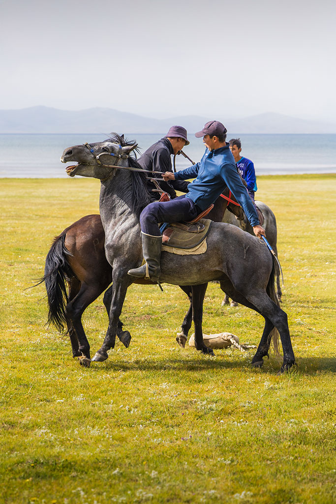 Actiefoto van paardenruiters in Kirgizië aan het Soň-Köl-meer die die de traditionele sport kok-boru spelen, door reisfotograaf Moments by Mark.