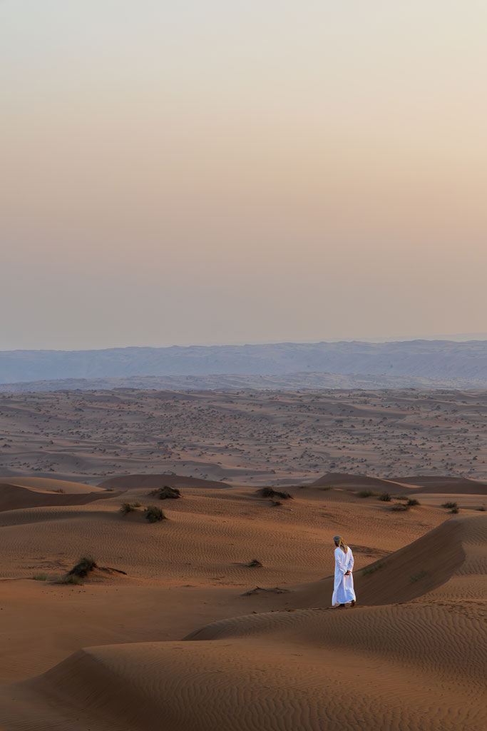 Foto van een eenzame lokale nomade in de een weids woestijnlandschap van Oman, door reisfotograaf Moments by Mark.