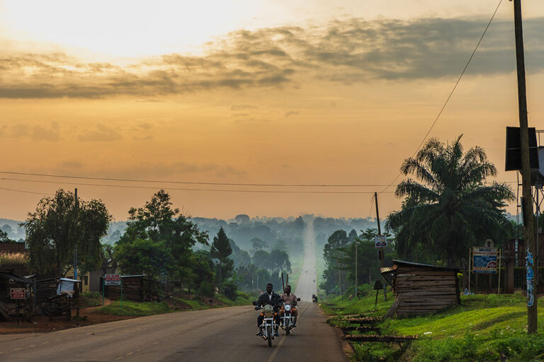 Motorrijders op de weg tijdens zonsopgang in Uganda door reisfotograaf Moments by Mark.