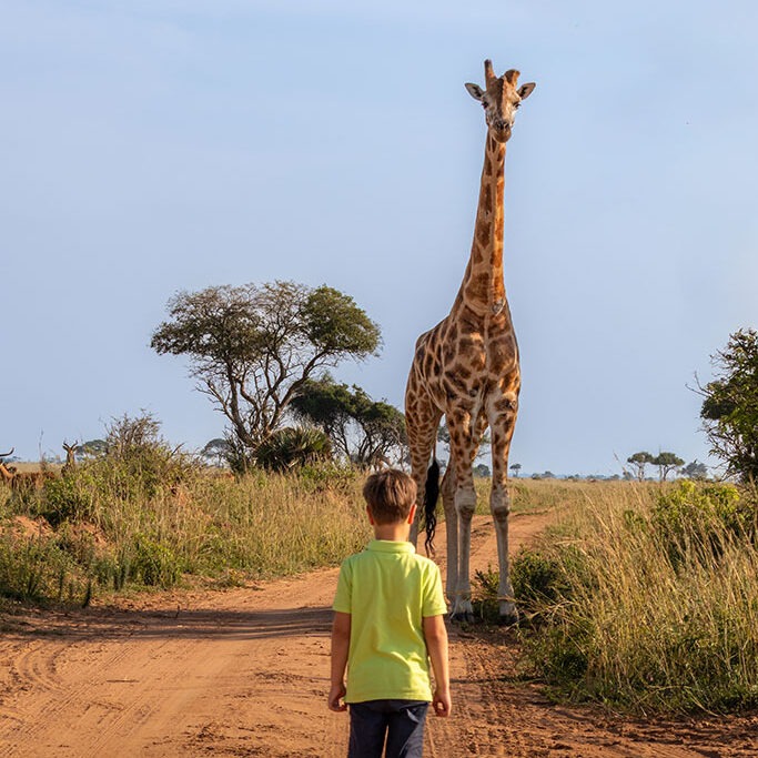 Foto van een ontmoeting van een jongen met een giraf in Oeganda, gemaakt door reisfotograaf Moments by Mark.